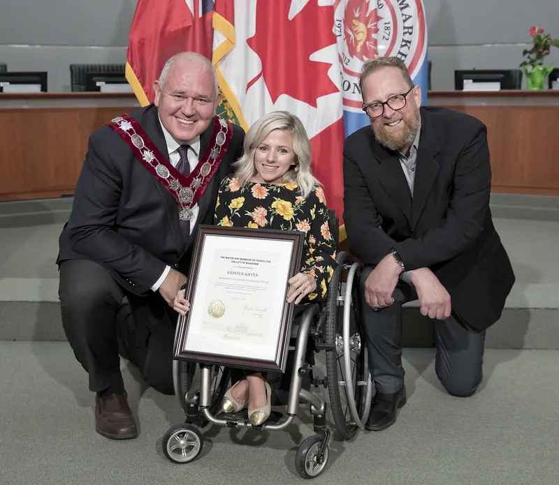 Posed picture with Award. From left to right: Markham Mayor Frank Scarpitti, Kristen Hayes, Past Recipient of the Markham Accessibility Award, and Barry Martin, Past Chair of the Markham Accessibility Advisory Committee.
