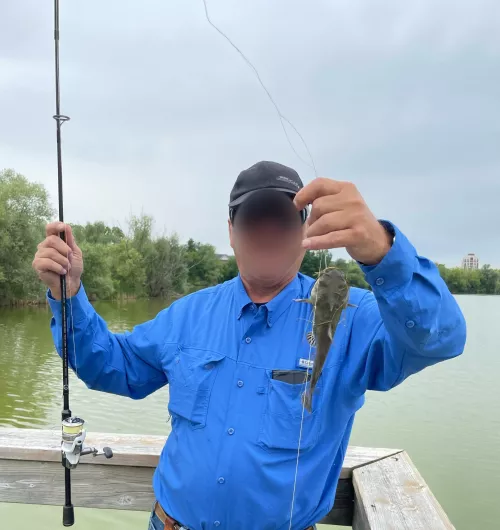 A man holding a catfish on a fishing hook he caught from Swan Lake