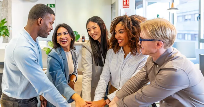 Happy business team joining hands in coworking office.